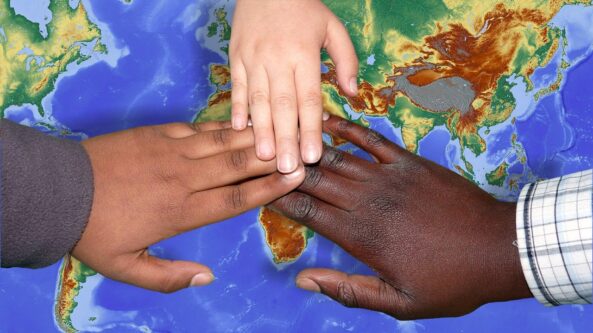 3 Hände vereinigen sich über einer Weltkarte
